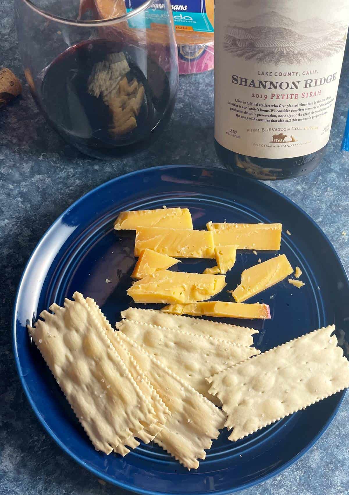 Gouda cheese on a blue plate with crackers, paired with a Petite Sirah red wine.
