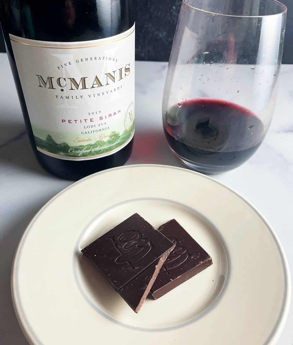 Two small pieces of dark chocolate on a little plate, served with McManis Petite Sirah wine.