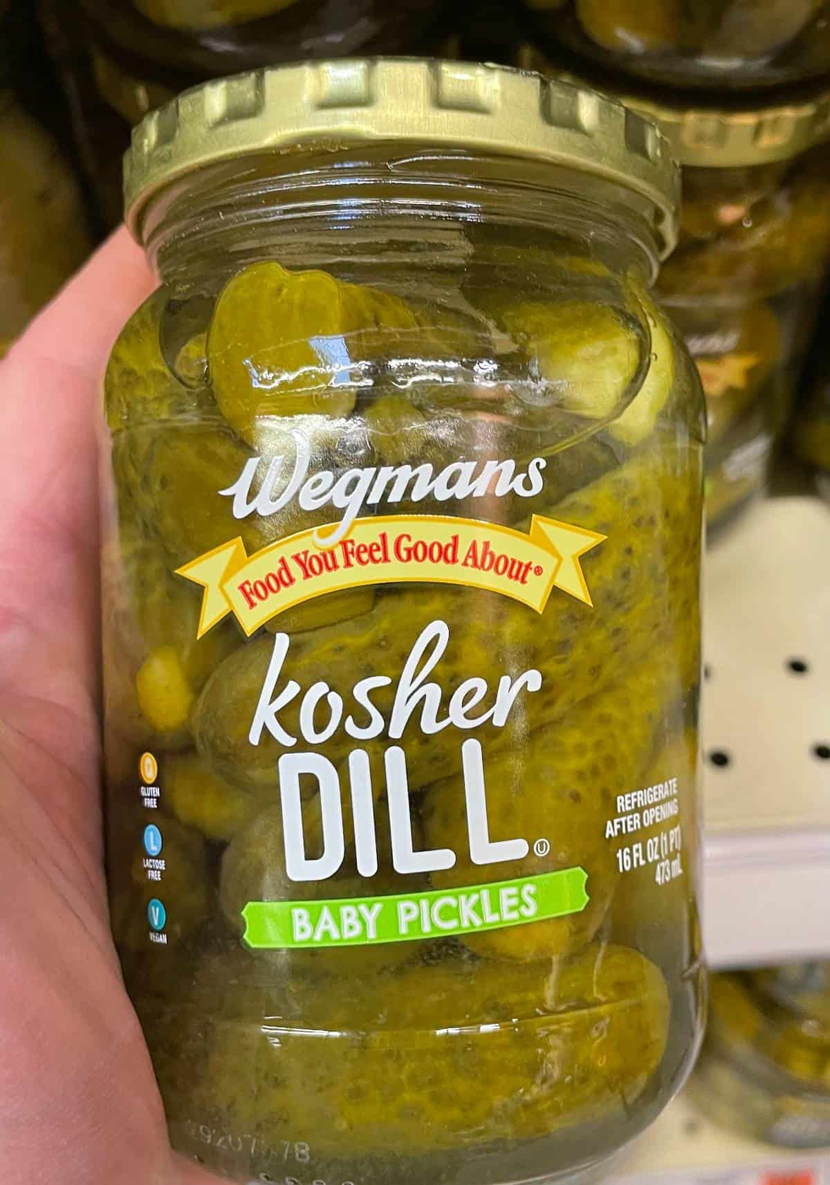 hand taking a jar of Wegman's kosher dill pickles from the shelf.