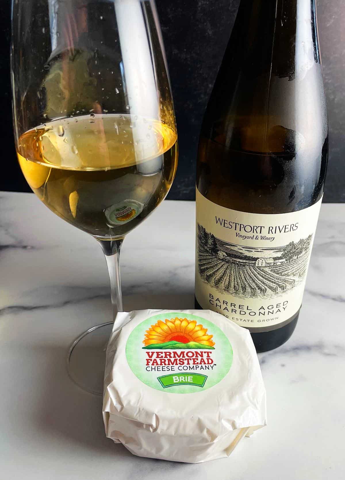 a package of Vermont Farmstead Brie along with a bottle and glass of Westport Rivers Chardonnay.