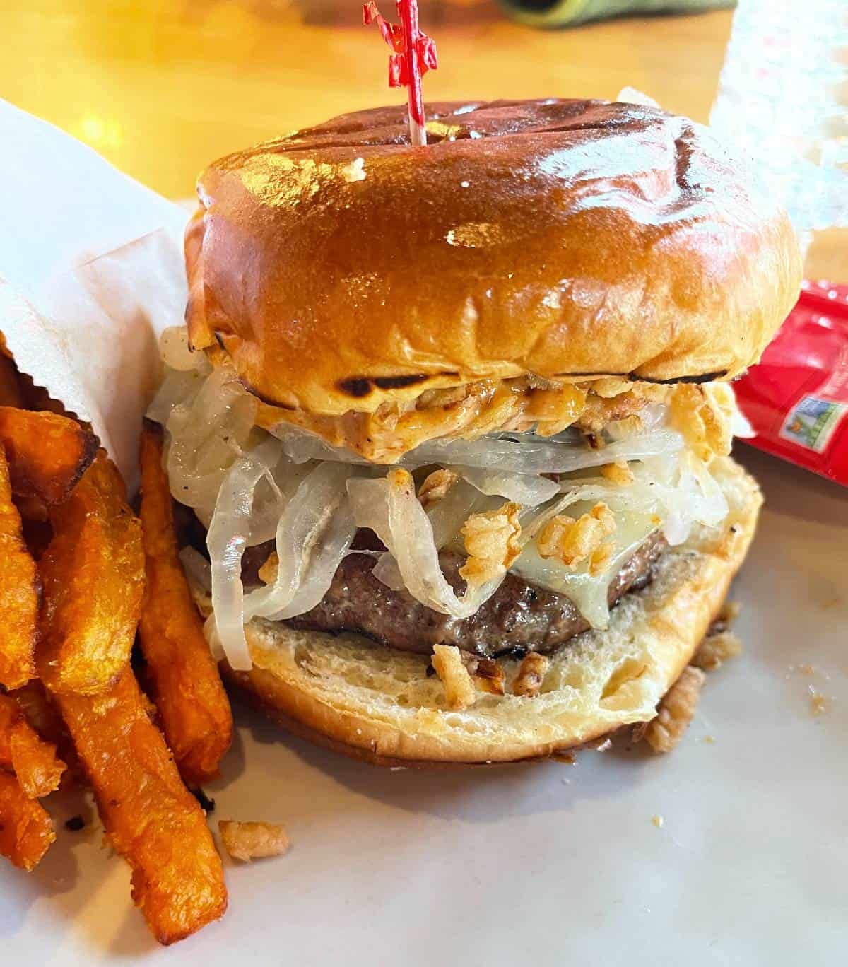 A cheeseburger on a bun, with sautéed onions and a side of sweet potato fries.