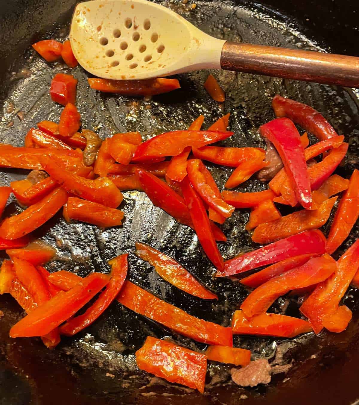 slice red bell peppers cooking in a black skillet.
