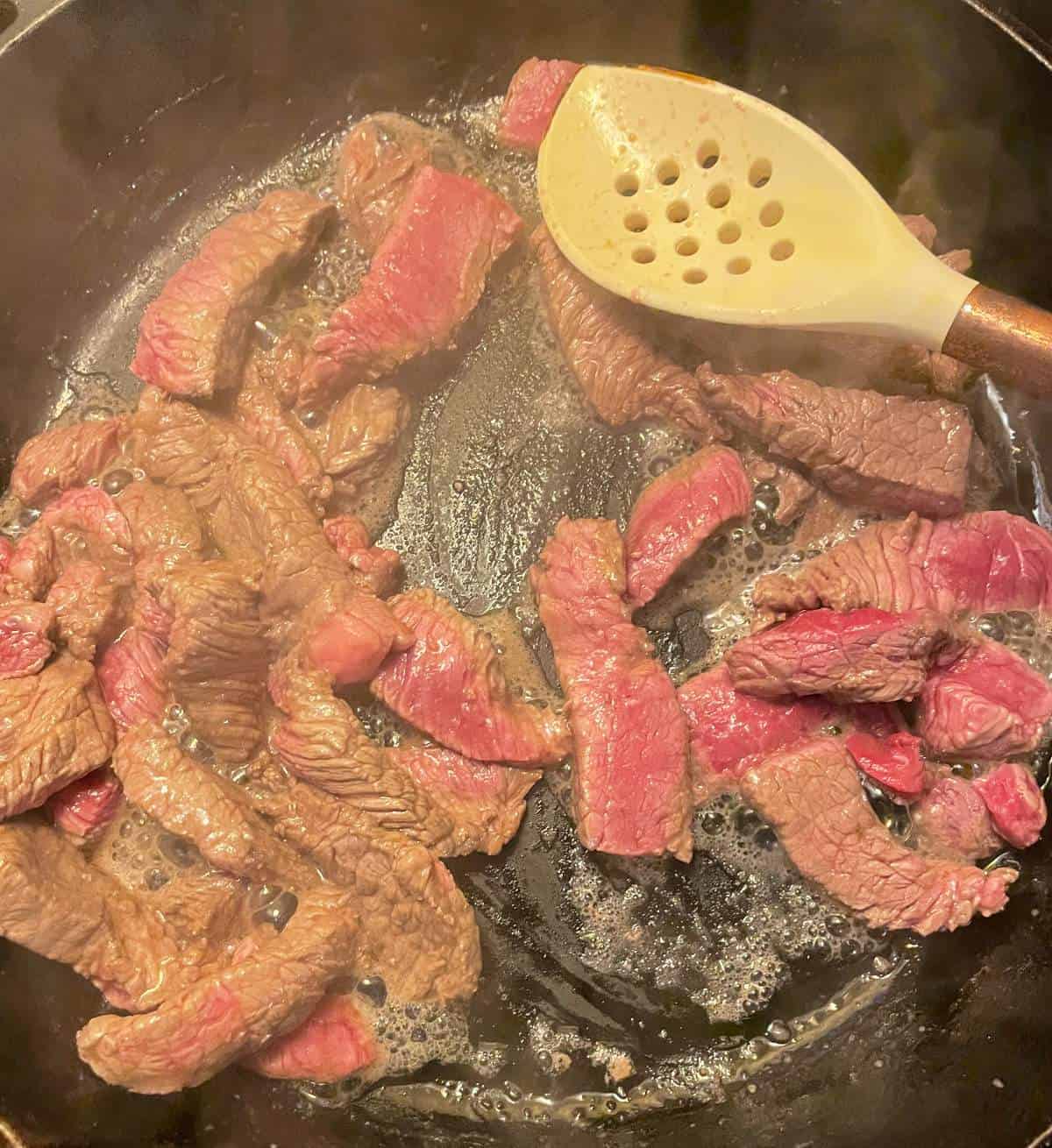 stir-frying thinly cut steak in a black skillet.