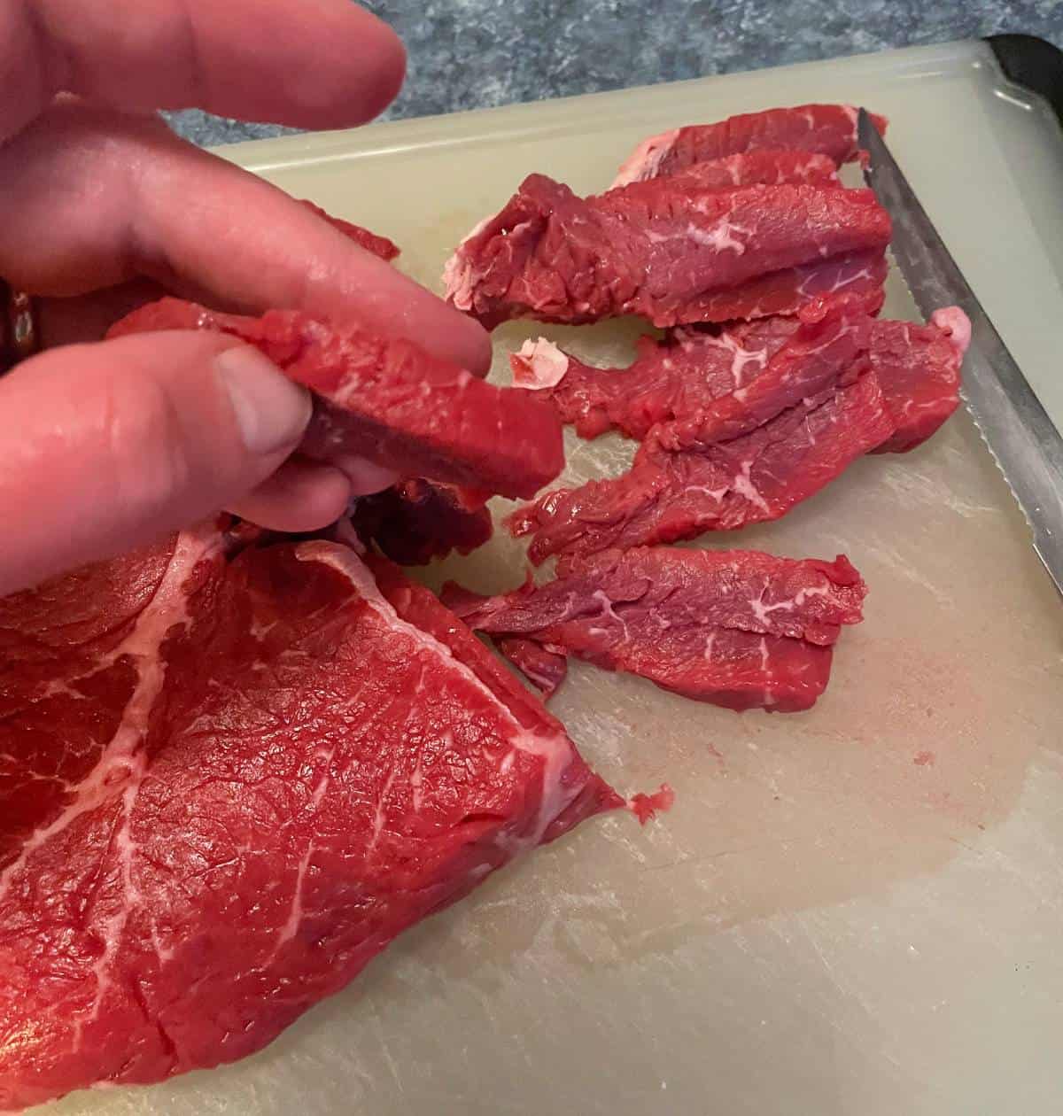 slicing raw sirloin steak on a cutting board.