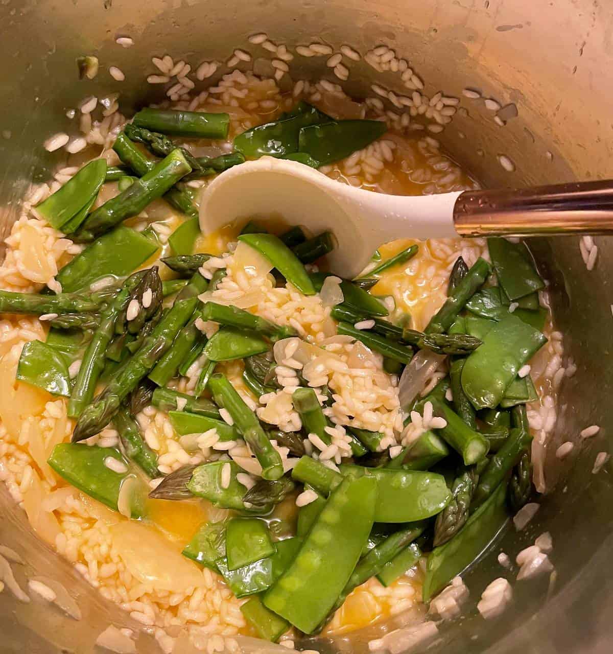 adding asparagus and peas to a pot of risotto.