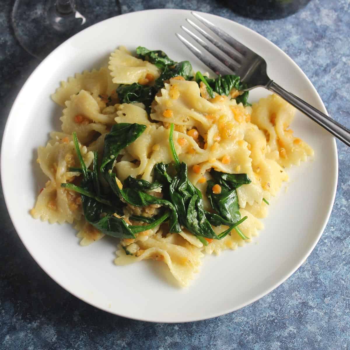 white plate with farfalle pasta with red lentils, ginger and spinach.