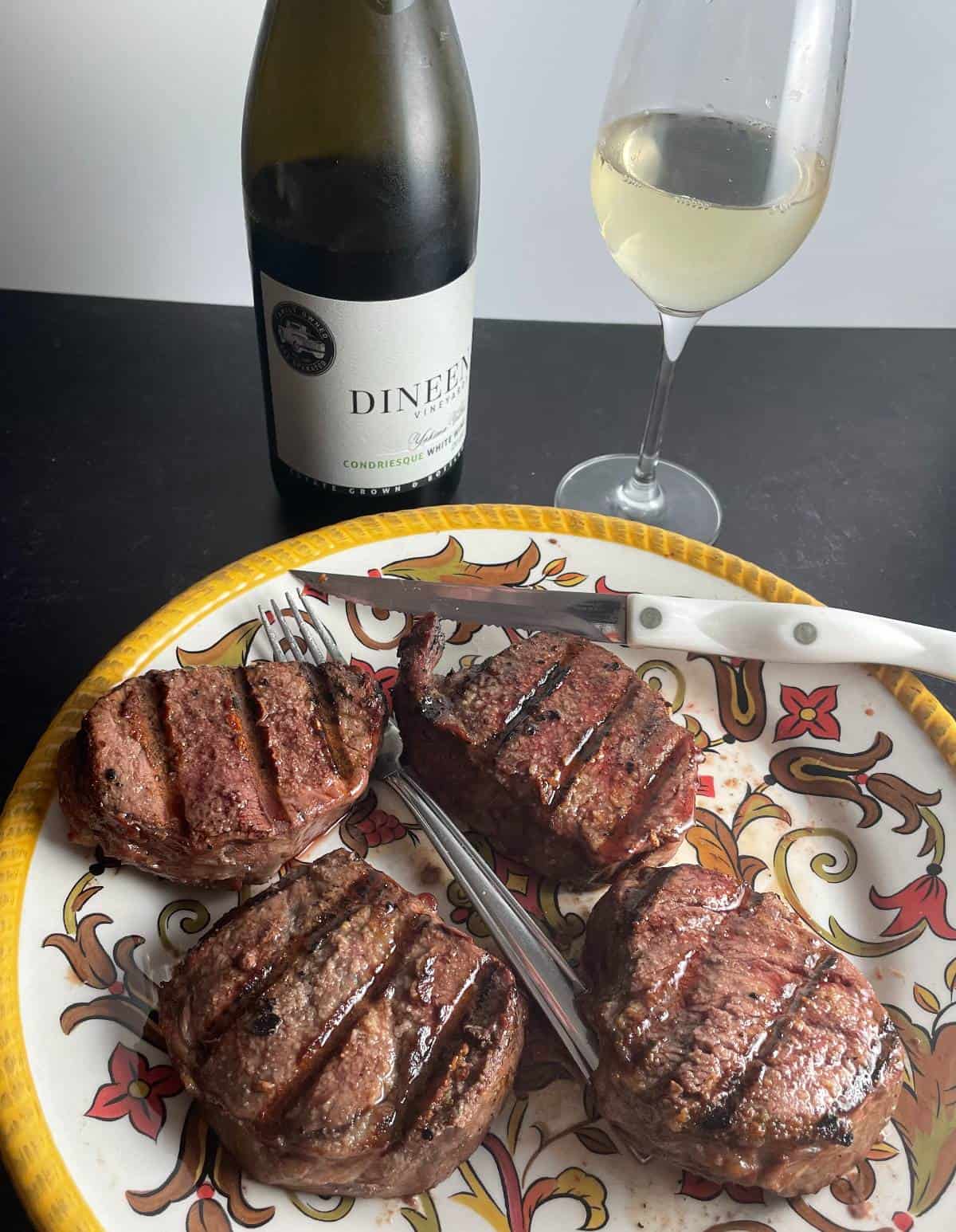 A platter of filet mignon with a bottle and glass of white wine in the background.