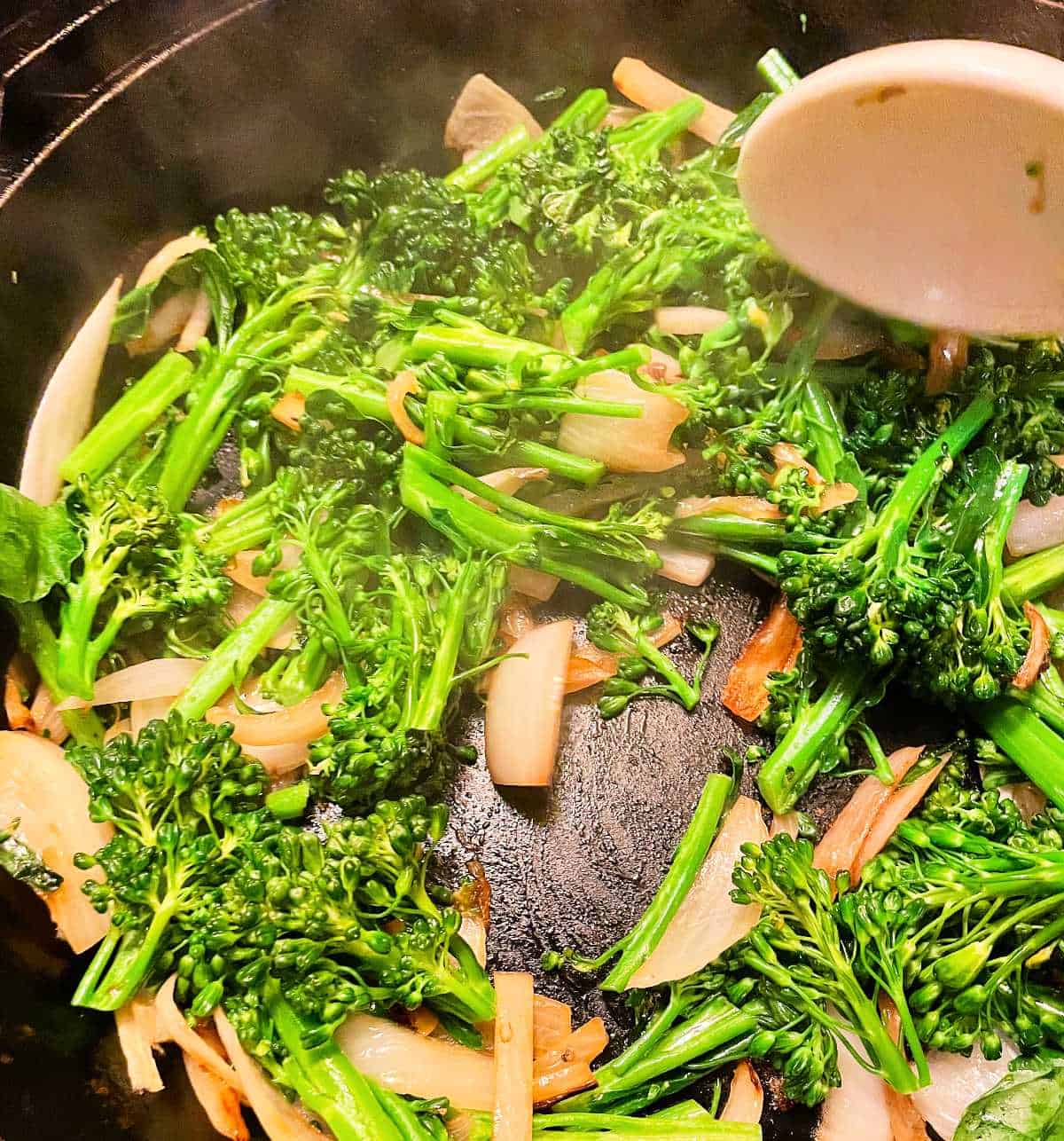 Stirring broccolini with onions in a black skillet. 