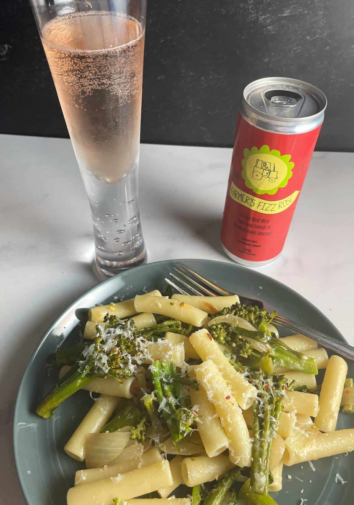 broccolini pasta served with a sparkling rosé wine. The can of this farmer's fizz wine is alongside the glass and plate.