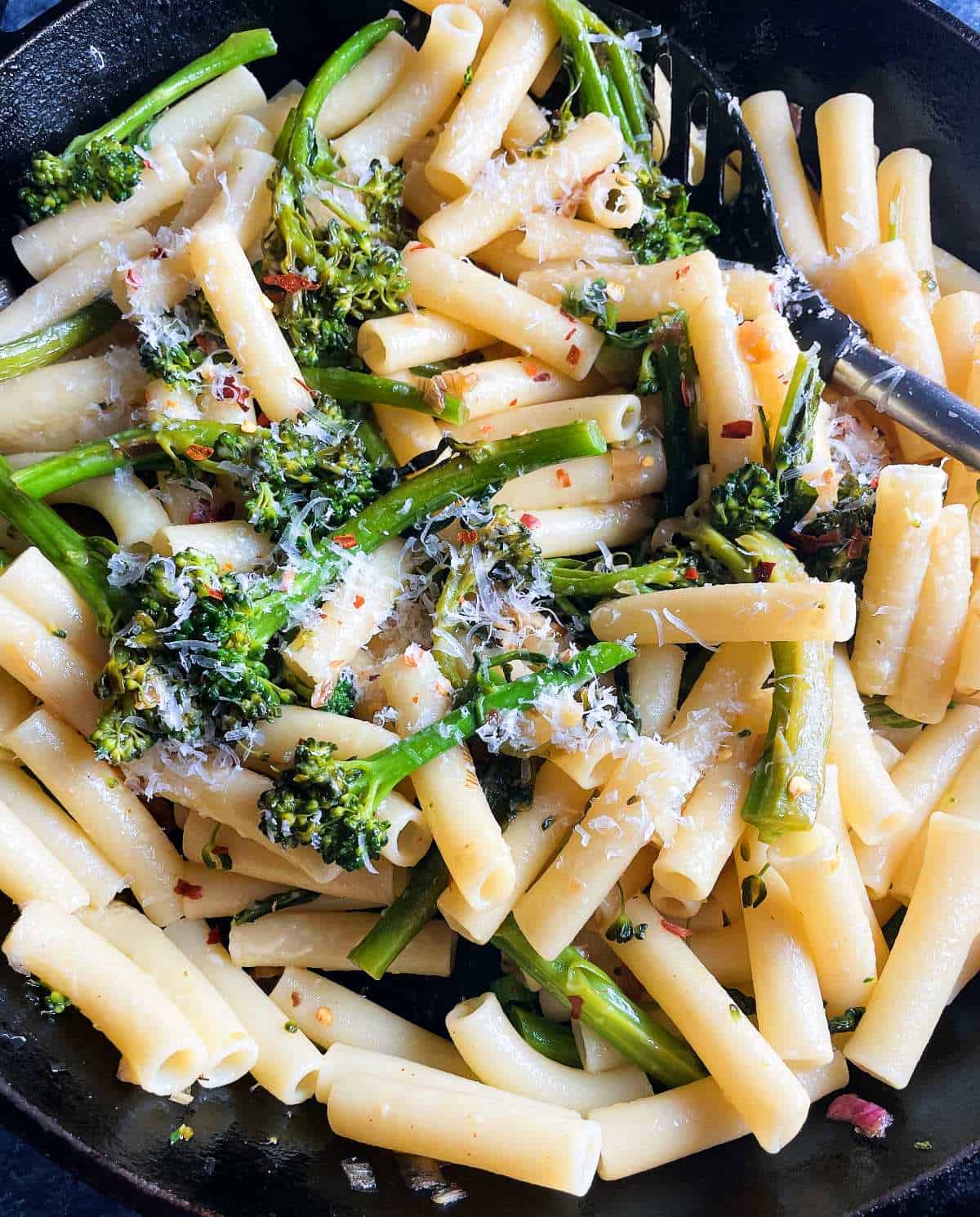 stirring ziti pasta with broccolini and cheese in a skillet.