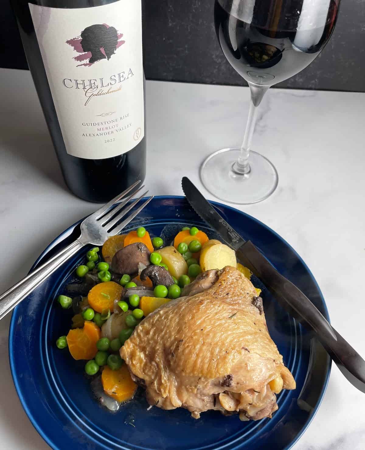 a braised chicken thigh plated with vegetables and served with a bottle of Merlot in the background.