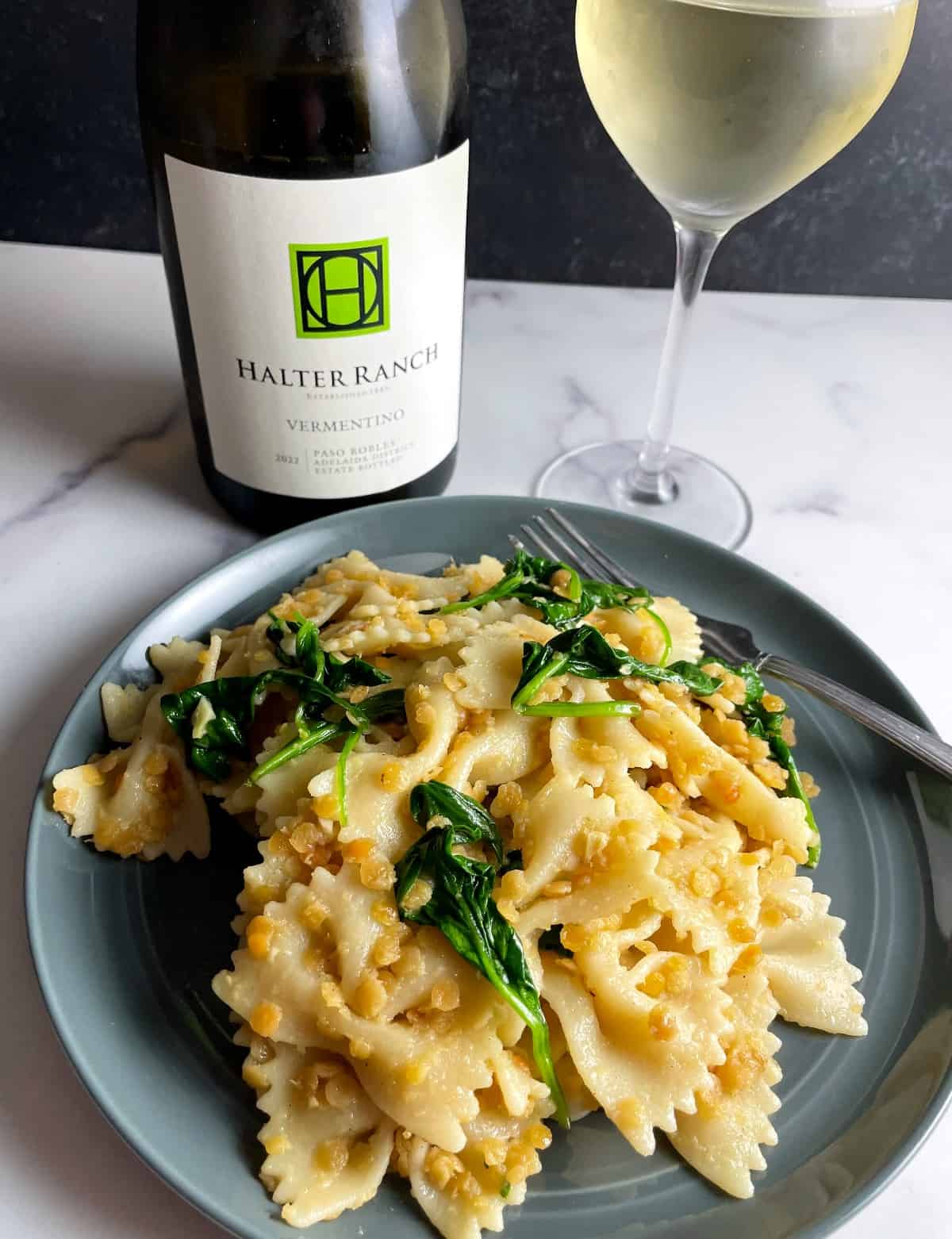 Bottle and glass of Halter Ranch Vermentino, served with a plate with bowtie pasta with red lentils and spinach.
