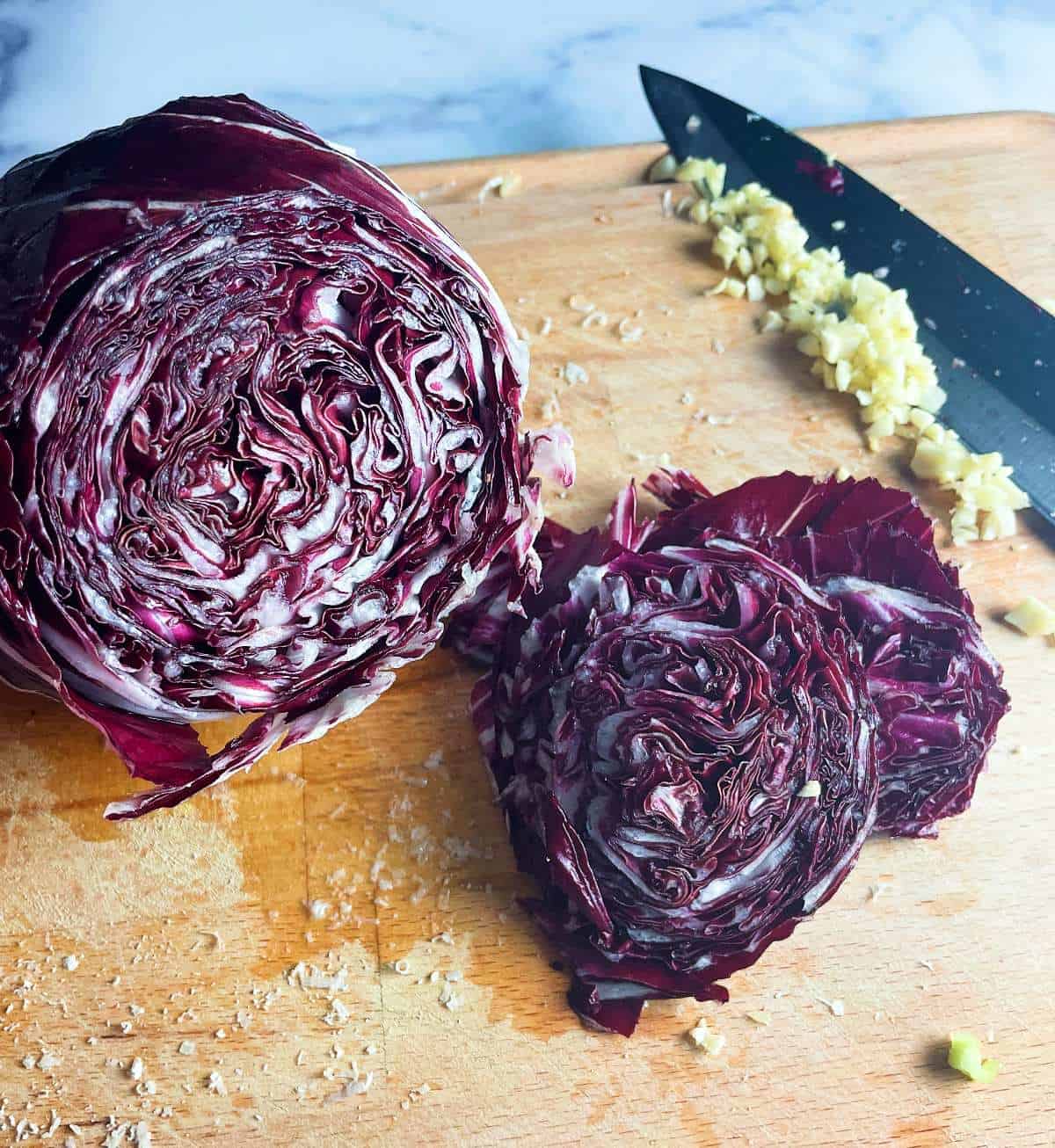 A head of radicchio on a chopping board, with one section cut off and set to the side. Minced garlic in the background.