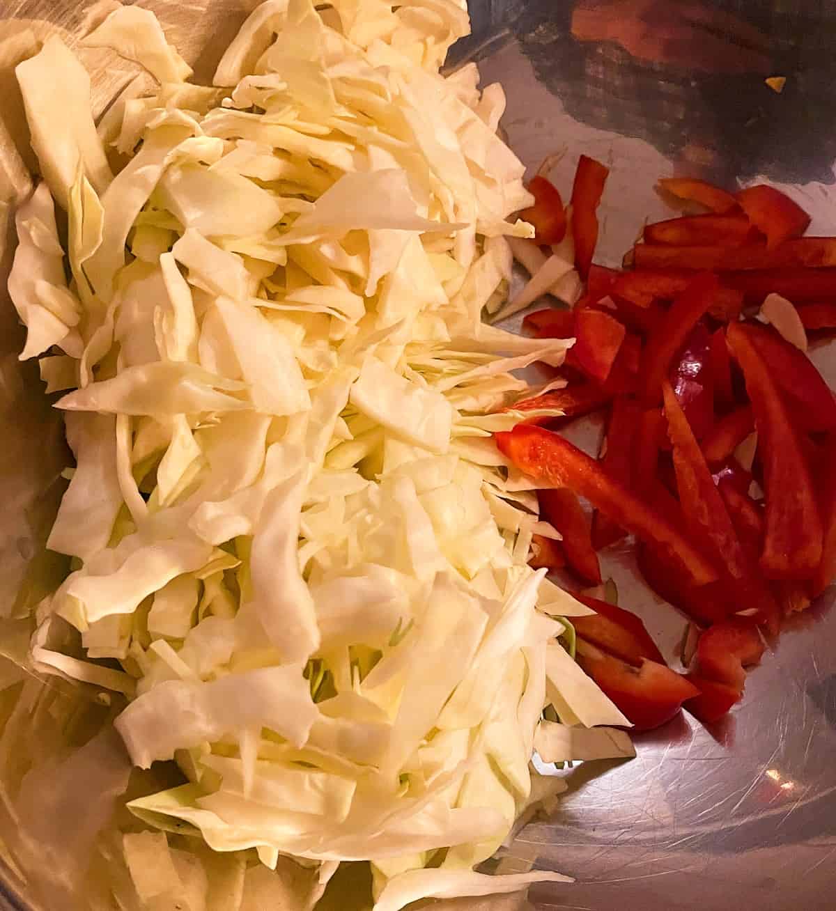 chopped cabbage and red bell peppers next to each other in a silver bowl.