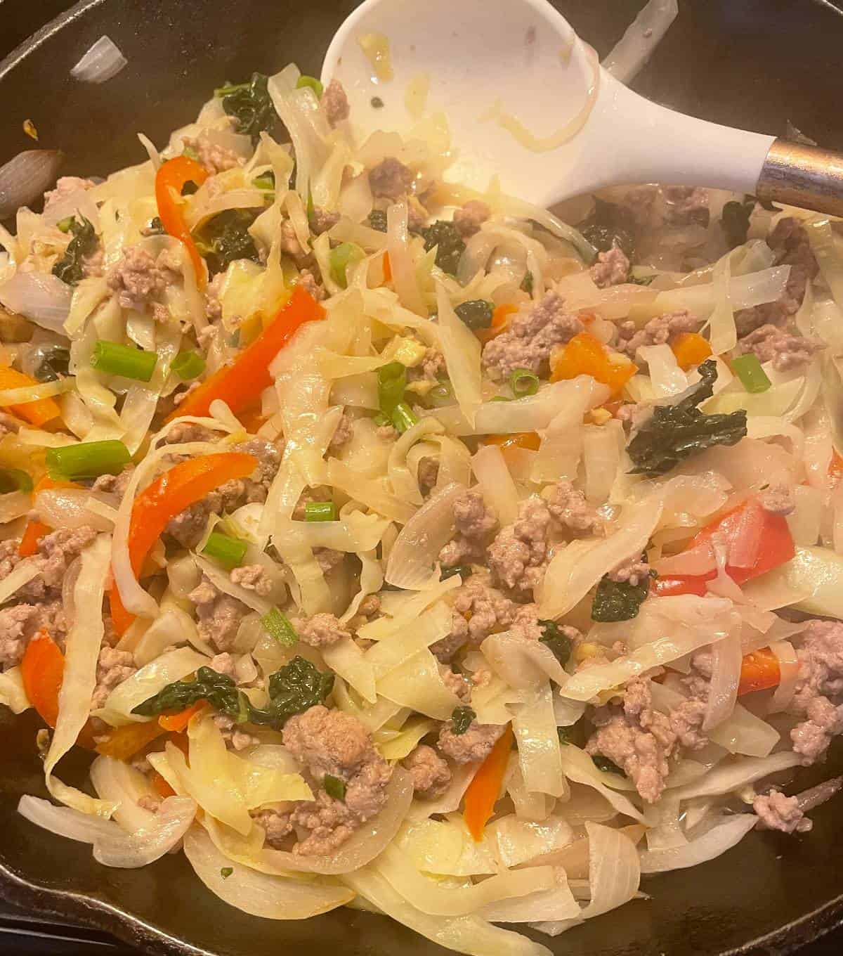 pork and cabbage stir-fry being stirred in a large skillet.