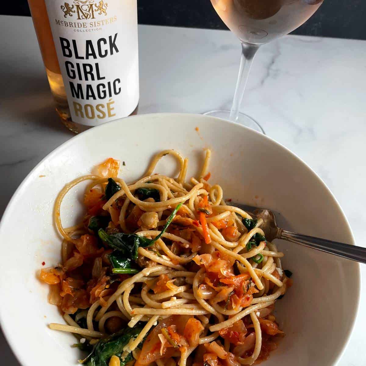 Bowl of kimchi spaghetti with bottle of Black Girl Magic rosé in the background.