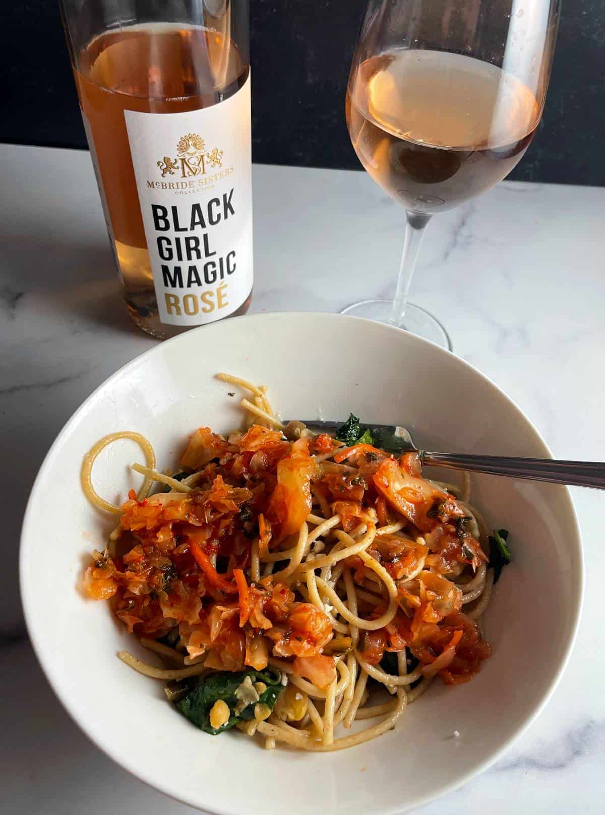 Bowl of kimchi spaghetti with bottle and glass of Black Girl Magic Rosé