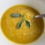 Roasted Acorn Squash Soup in a white bowl, topped with fresh sage leaves.