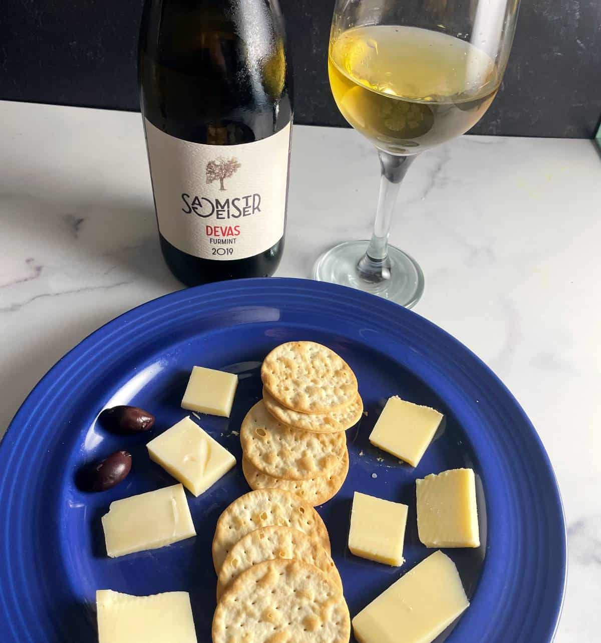 cheese plate with crackers, served with a Furmint white wine bottle and glass of the wine.