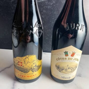 Two bottles of wine side by side. One is an Apremont white wine, the other is a Cotes du Jura red.