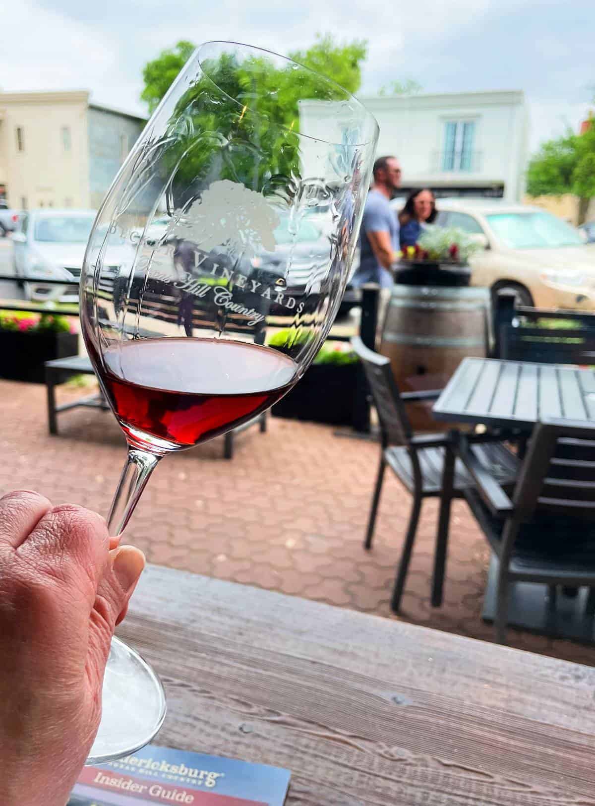 a hand holding a glass of red wine, which is catching the natural light from a window.
