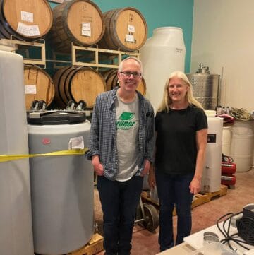 Salado Winery Owner / Winemaker June Ritterbusch with David Crowley, posing by wine tanks.