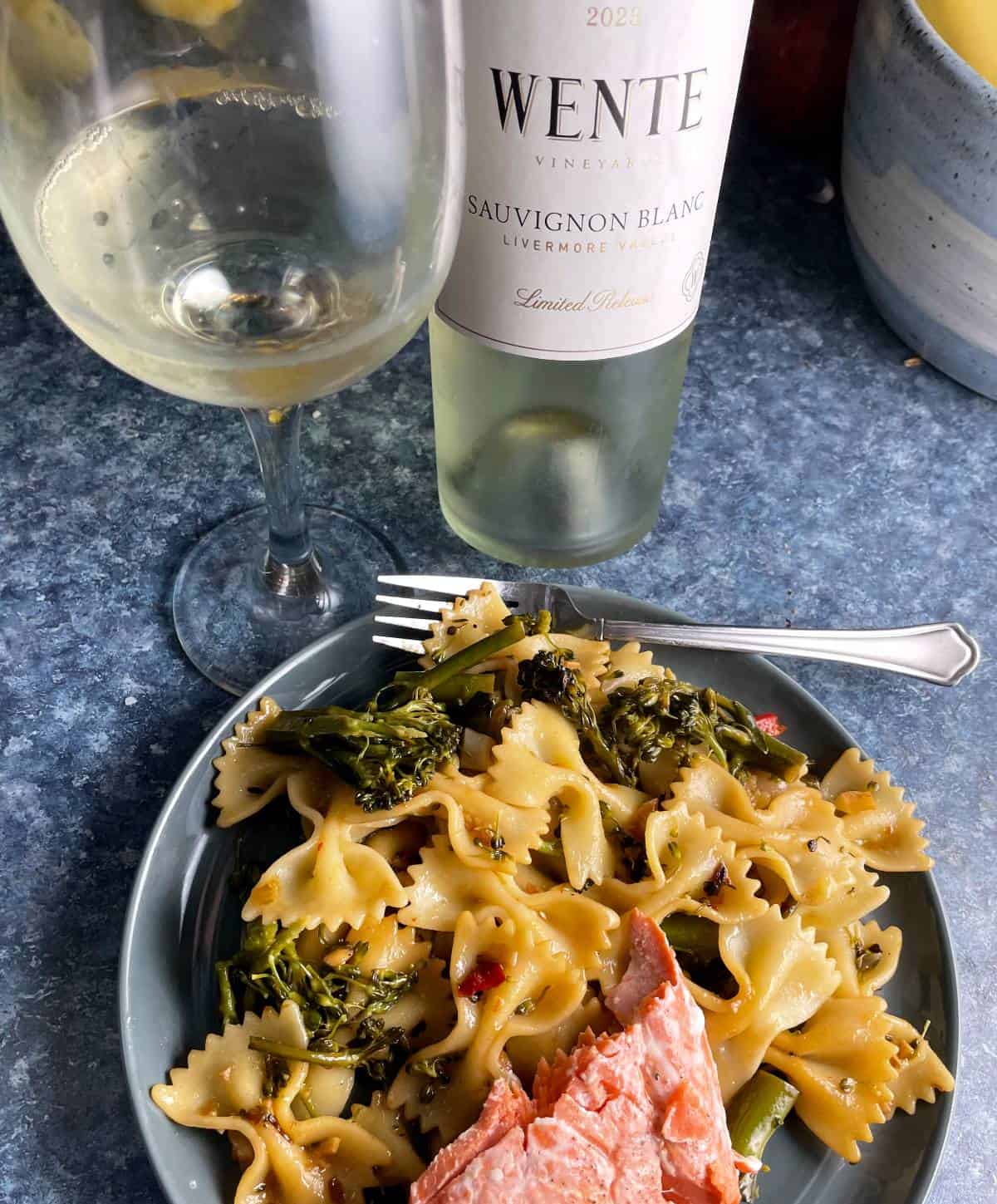 Broccolini pasta served with salmon and a Sauvignon Blanc wine in the background.