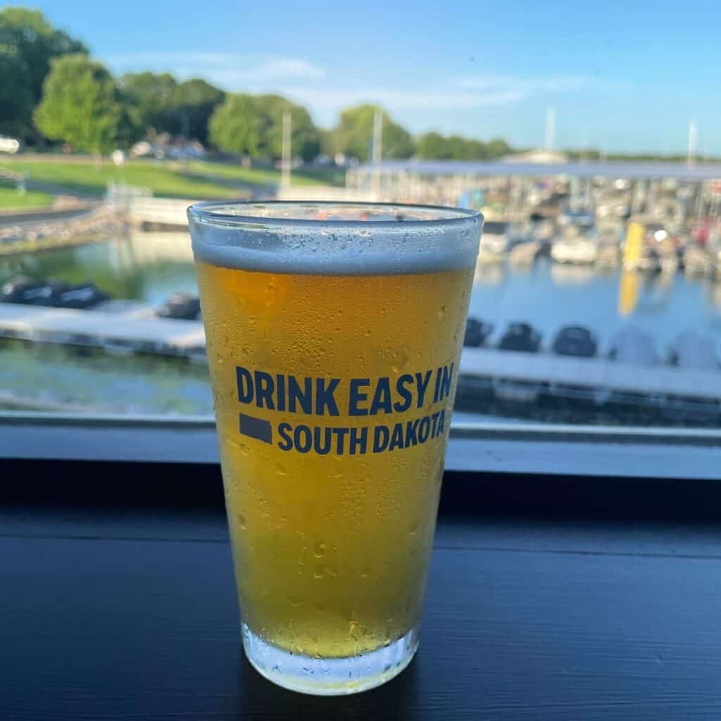 Pint of beer in a glass that says Drink Easy in South Dakota with a marina in th ebackground.