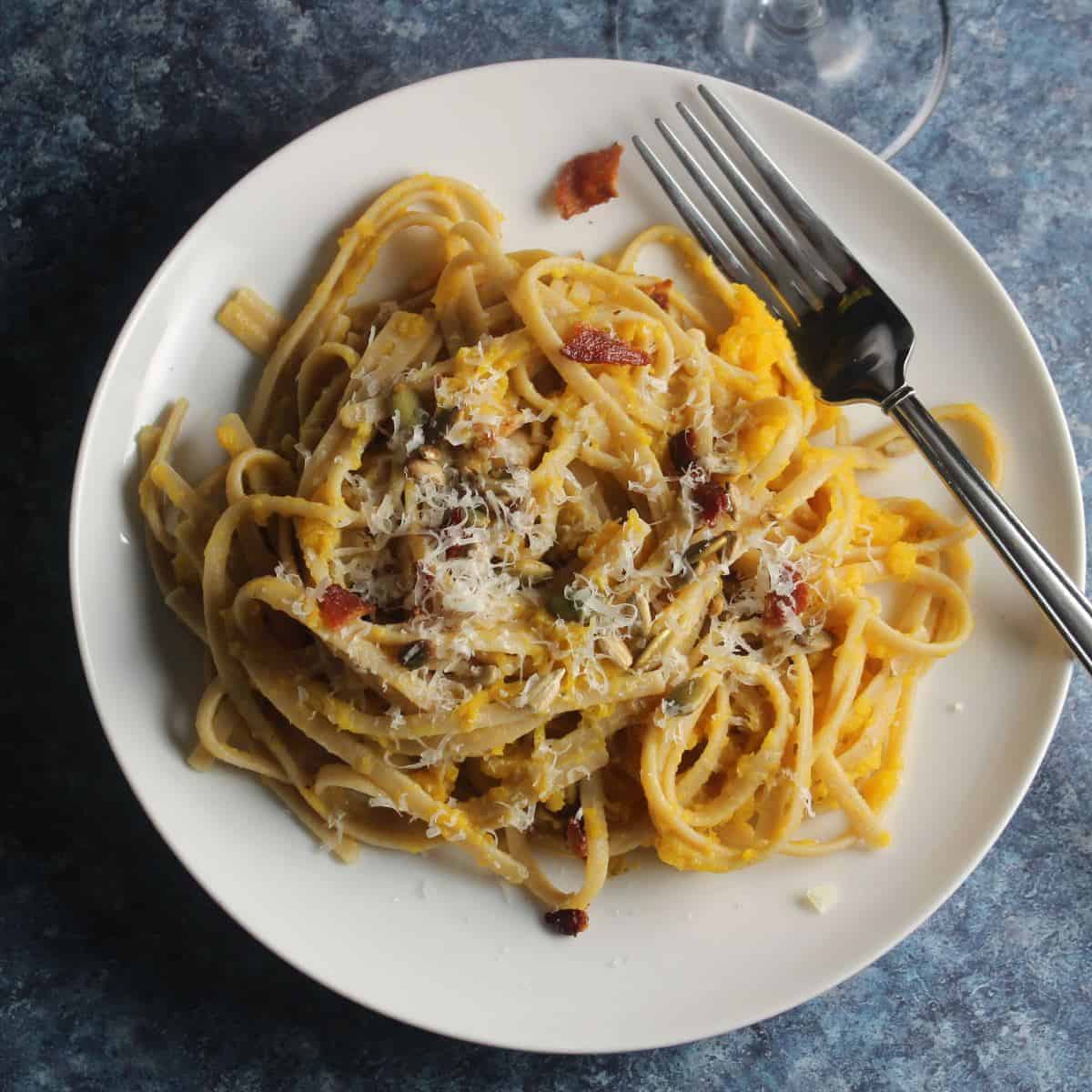 butternut squash pasta with bacon, served on a white plate.