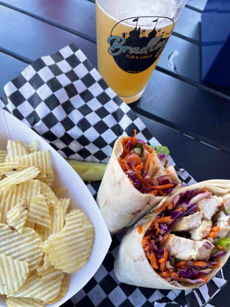 chicken wrap sandwich served with a side of chips and a beer.
