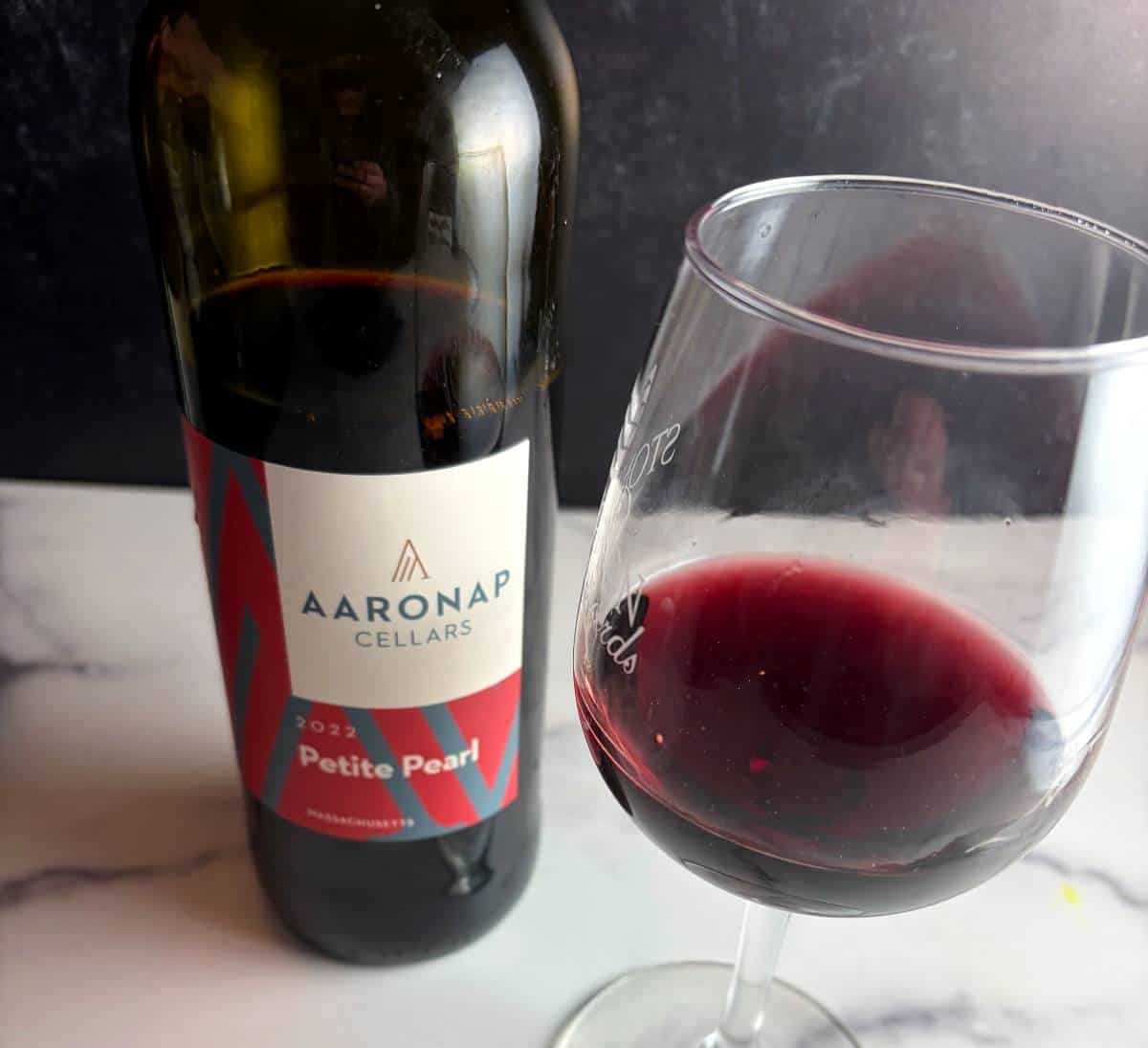 A bottle of Aaronap Cellars Petite Pearl with a glass of the red wine paired alongside it.