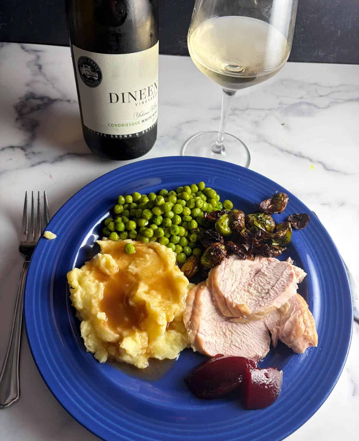 a turkey dinner, including mashed potatoes and cranberry sauce, served on a blue plate with a bottle of white wine in the background.