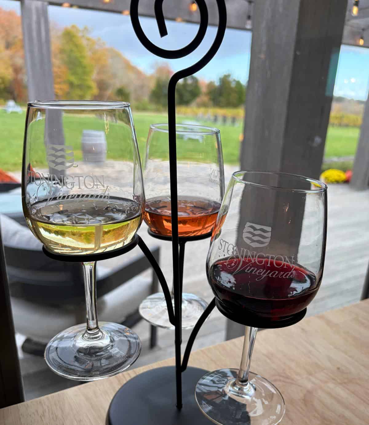 three tasting pours of wine displayed on a table with a view of the vineyard visible through the window.