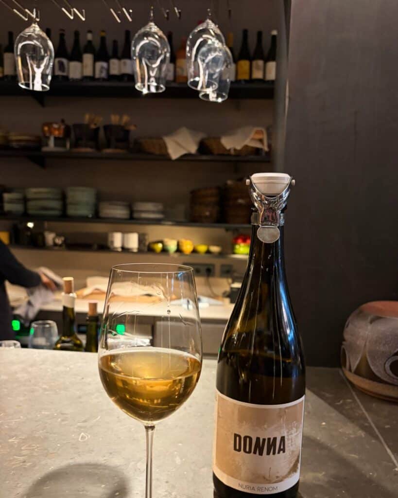 Photo of Núria Renom "Donna" — natural sparkling Chardonnay with glasses hanging upside down in the background. At Mon Vinic wine bar in Barcelona.