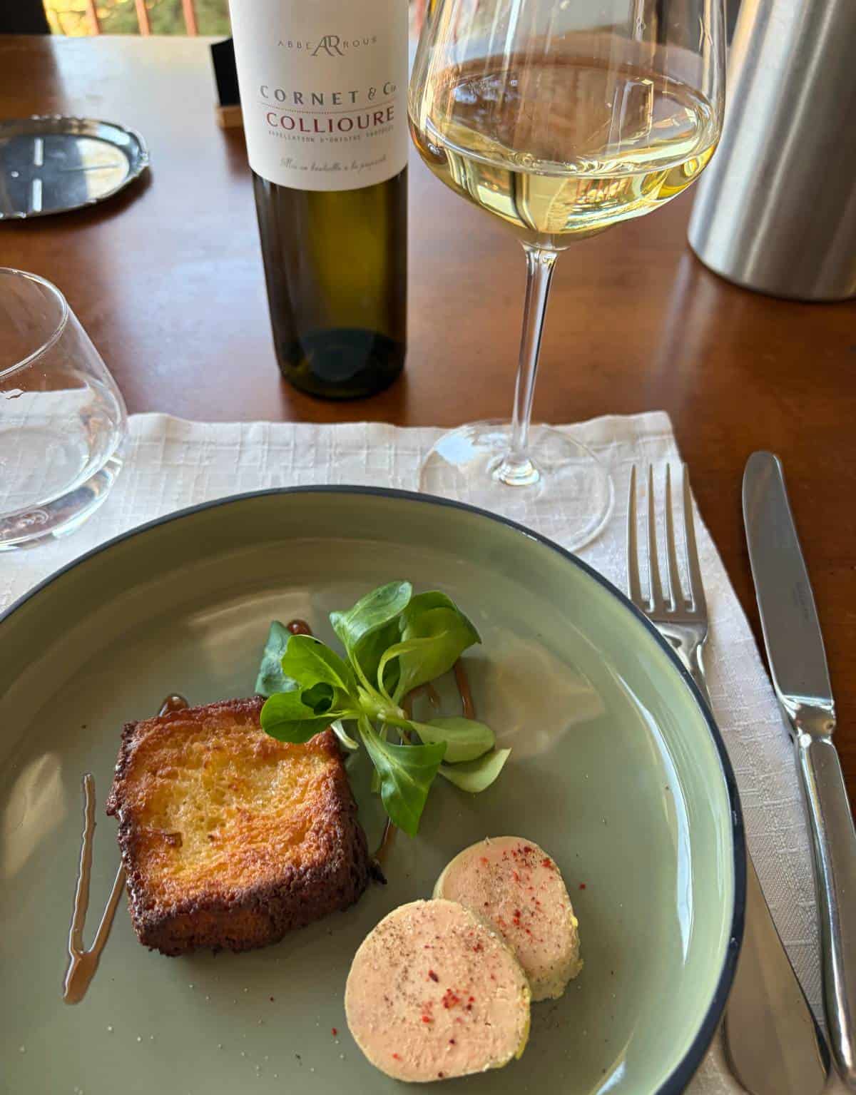 foie gras and toast on a plate, with white wine in the background.