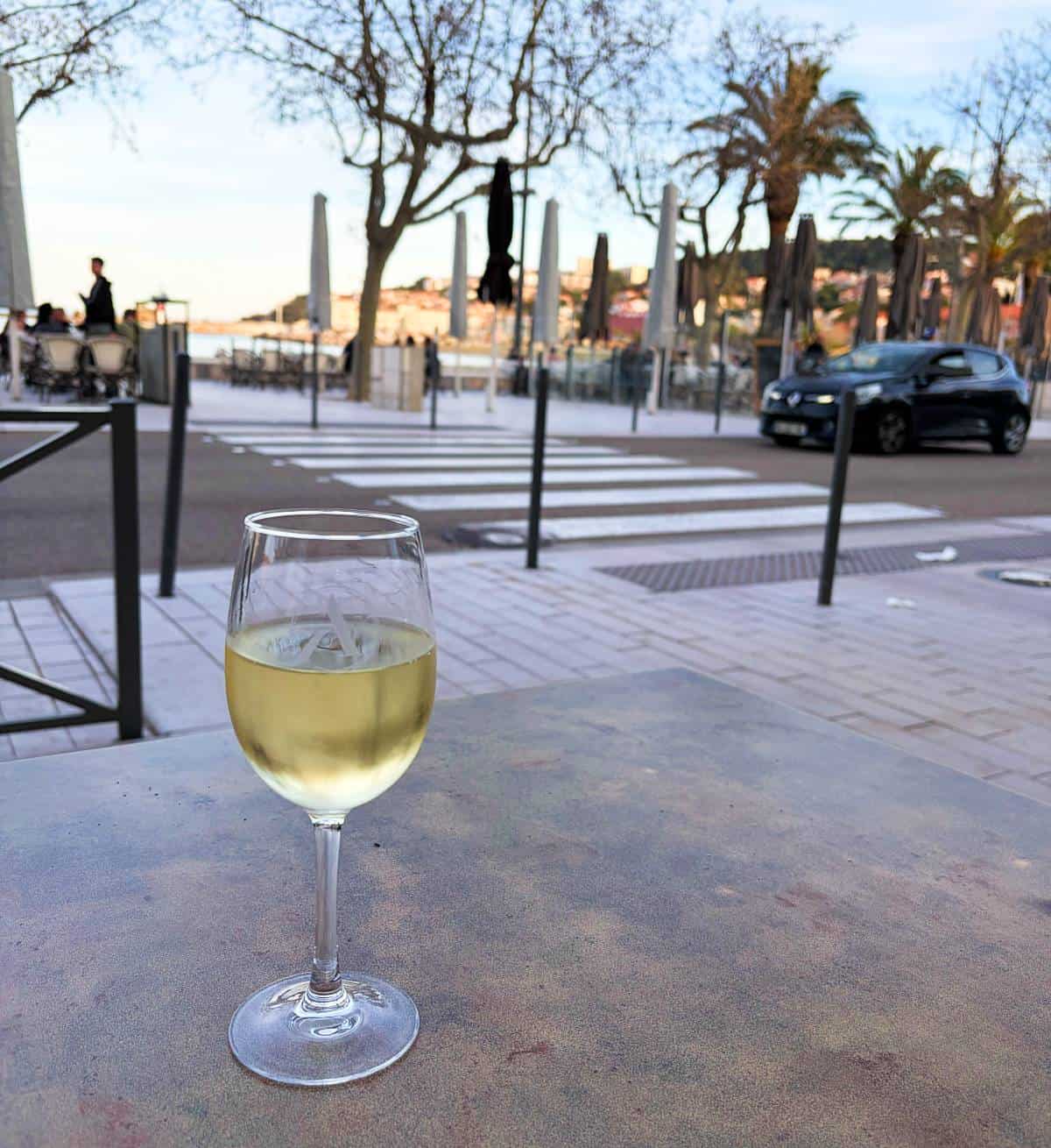 a glass of white wine on a cafe table with a few palm trees in the background.