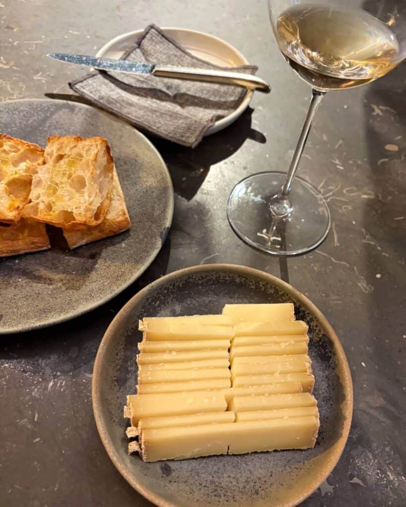 photo of sliced cheese with toasted bread to the left and a glass of white wine on the right.