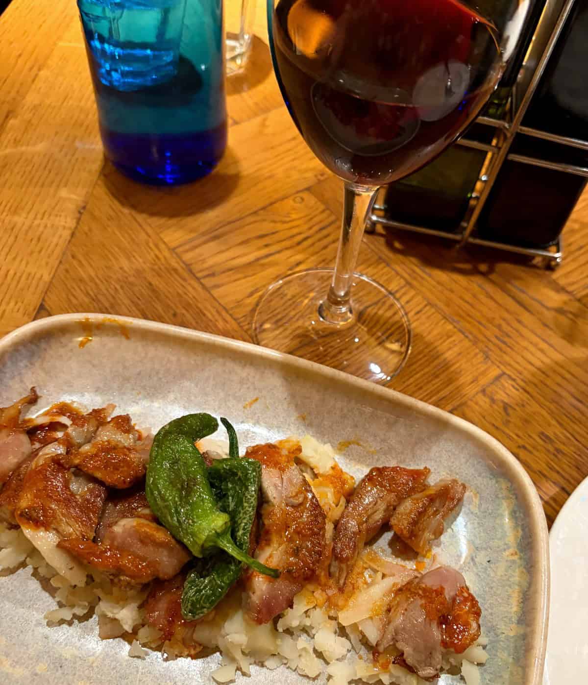 a plate with pork and green peppers, and a glass of red wine in the background.