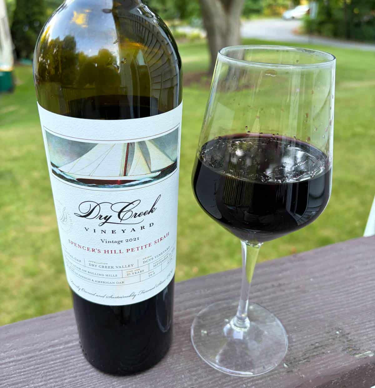 Dry Creek Petite Sirah red wine -bottle with a glass poured next to it,grass in the background.