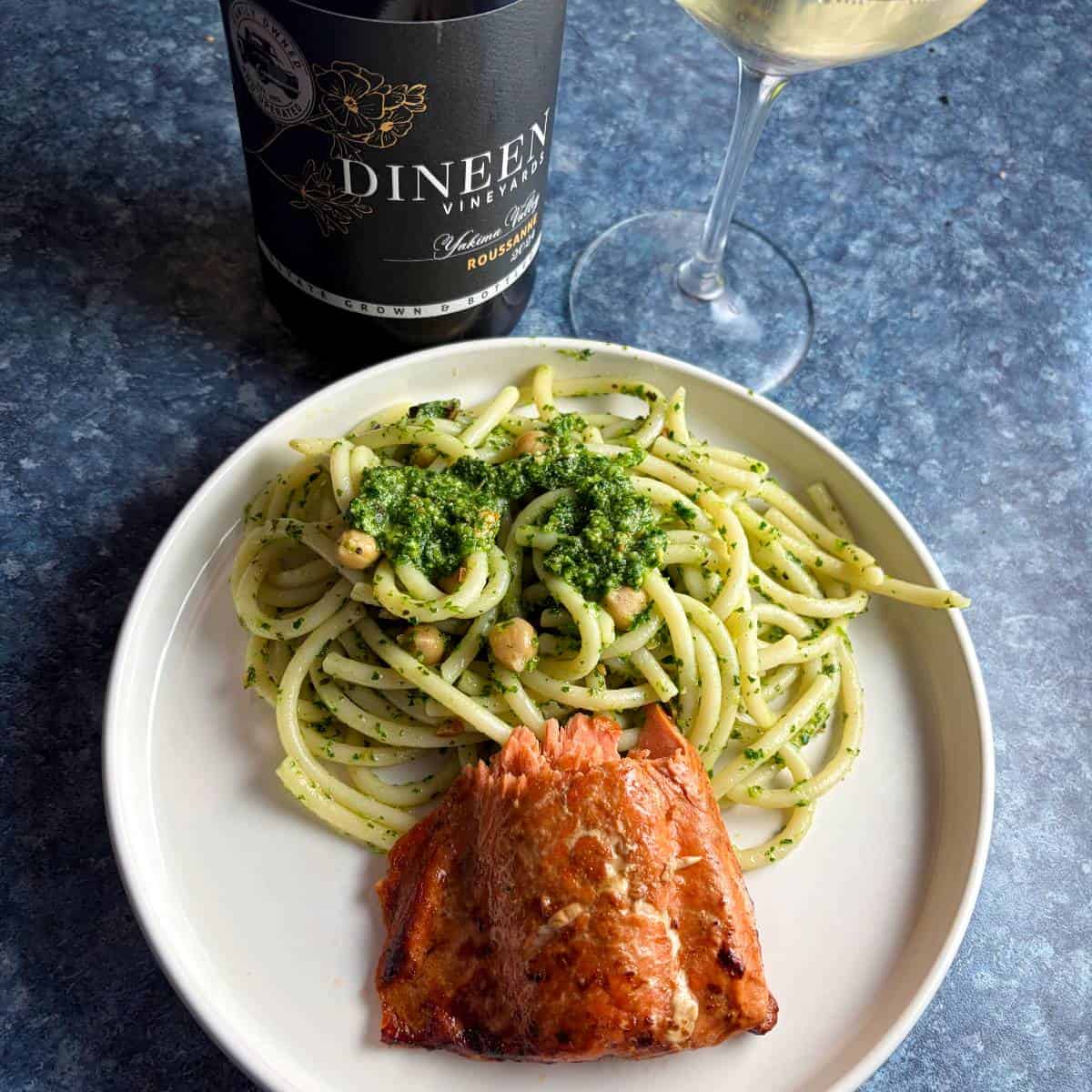 a piece of salmon plated with pesto topped with pesto, served with a white wine.