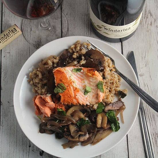 salmon served over farro with mushrooms, and a red wine next to the plate.