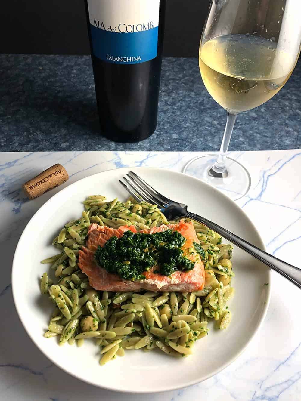 salmon served on a bed of orzo, topped with pesto. white wine in the background.